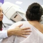 Técnica acompanha paciente durante exame de mamografia
