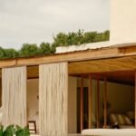 Varanda de casa de madeira e palha com rede, cercada de vegetação
