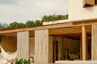 Varanda de casa de madeira e palha com rede, cercada de vegetação
