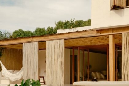 Varanda de casa de madeira e palha com rede, cercada de vegetação