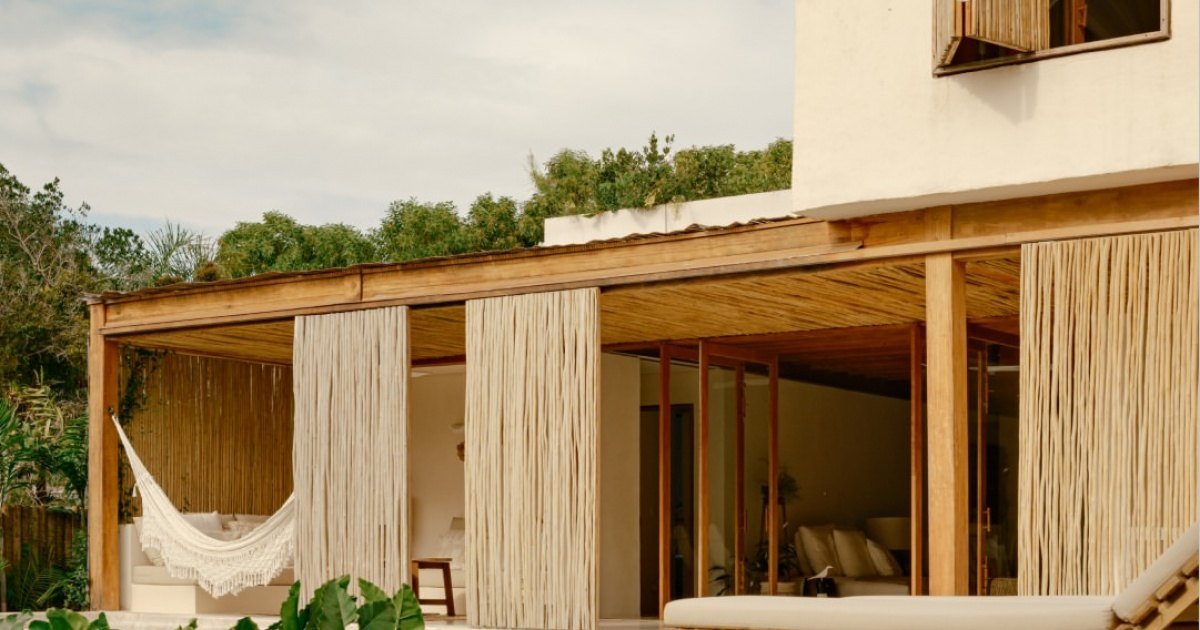 Varanda de casa de madeira e palha com rede, cercada de vegetação