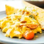 Prato de ovos mexidos cremosos com tomates ao lado