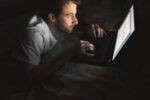Homem usando notebook à noite em posição curvada