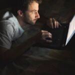 Homem usando notebook à noite em posição curvada