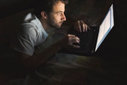 Homem usando notebook à noite em posição curvada