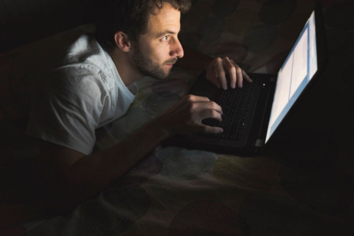 Homem usando notebook à noite em posição curvada