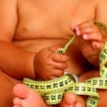 Barriga de criança com fita métrica enrolada na mão